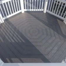 Empty wooden deck with white railing, casting shadows from the railing posts.