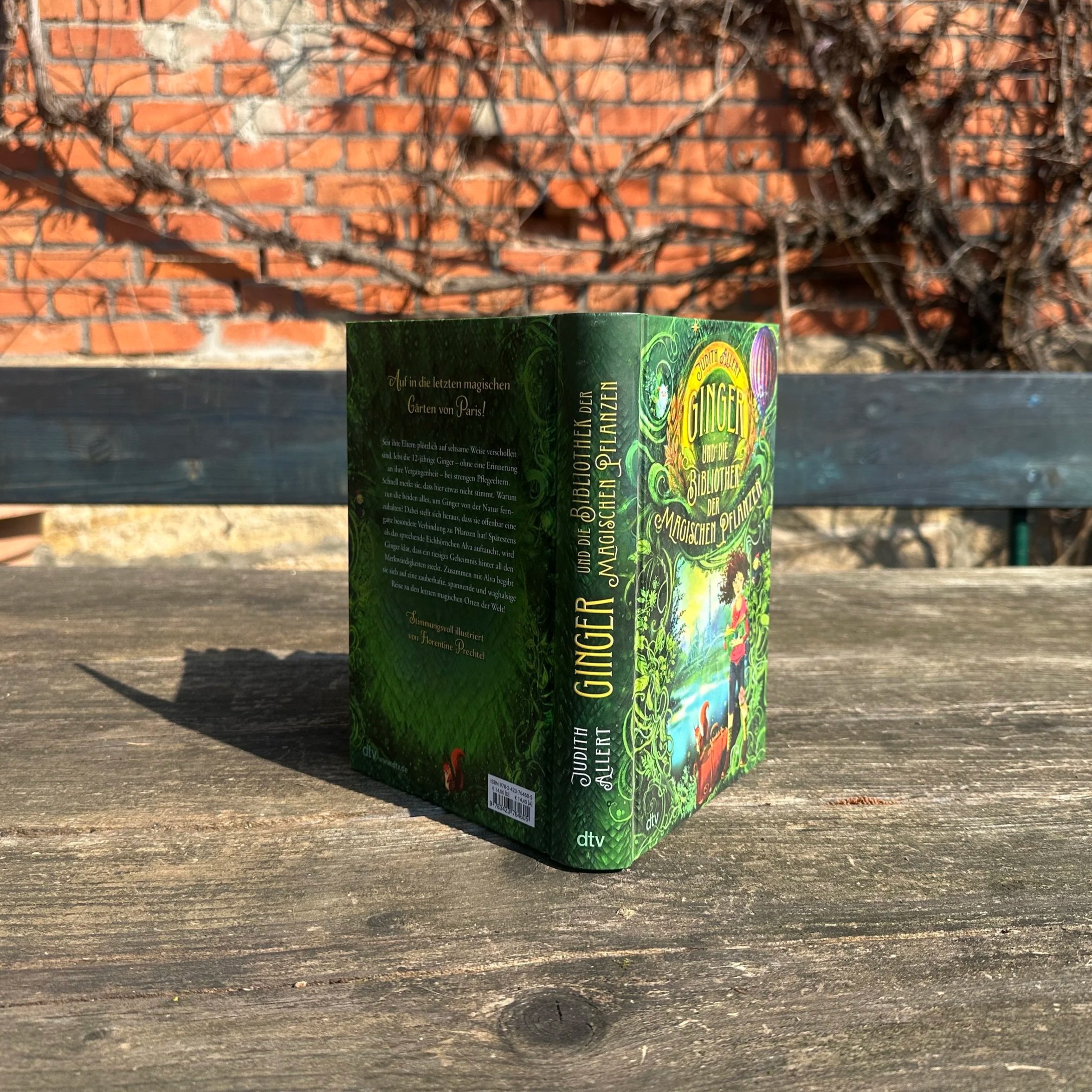 Das Buch "Ginger und die Bibliothek der Magischen Pflanzen" steht hochkant auf einem Holztisch.