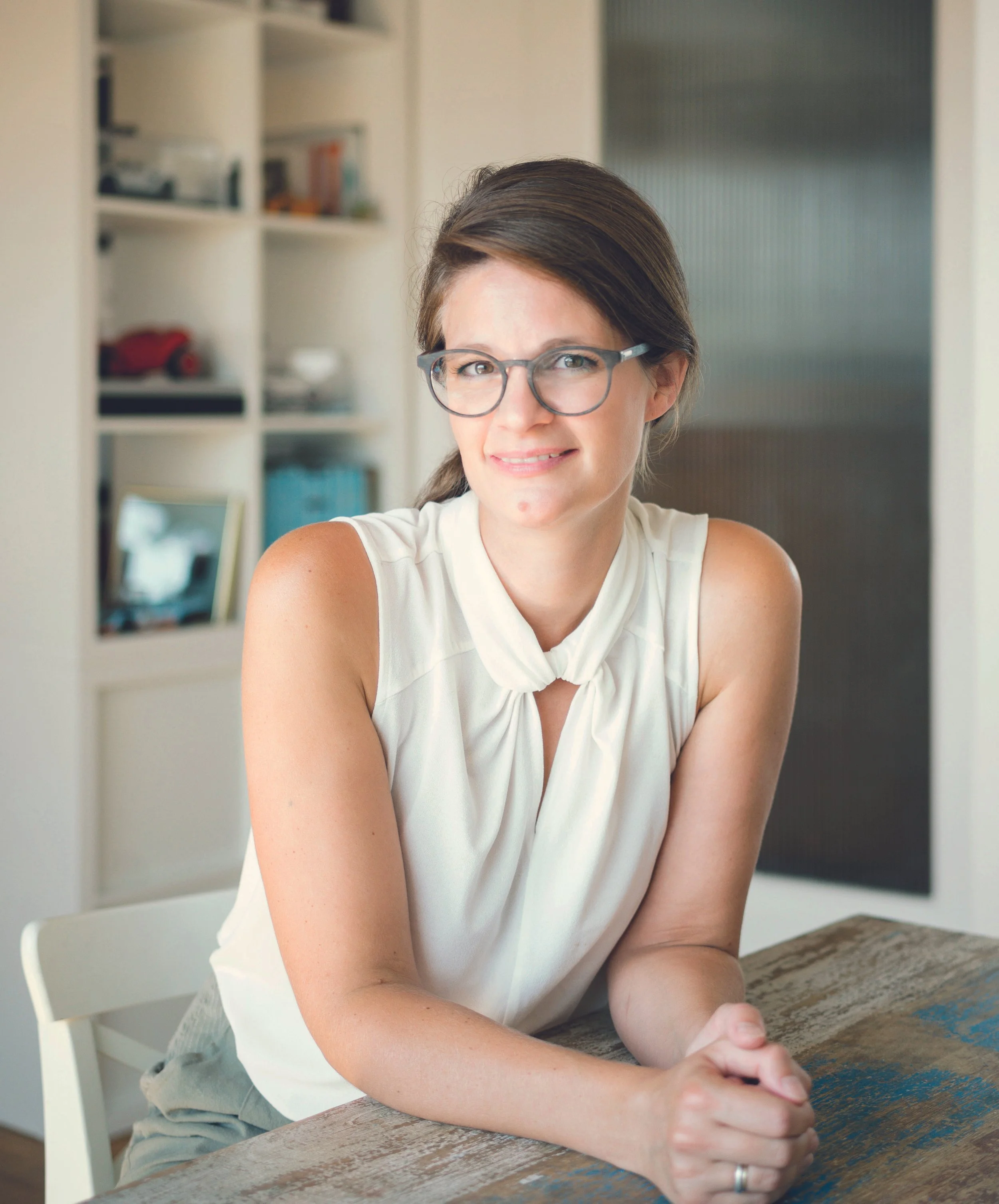 Anna-Lena Kühler mit Brille sitzt an einem Holztisch und lächelt.
