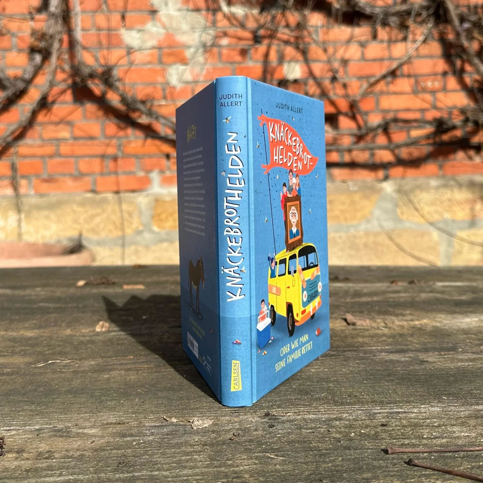 Ein Foto vom Buchrücken des Buchs "Knäckebrothelden". Es steht hochkant auf einem Holztisch."