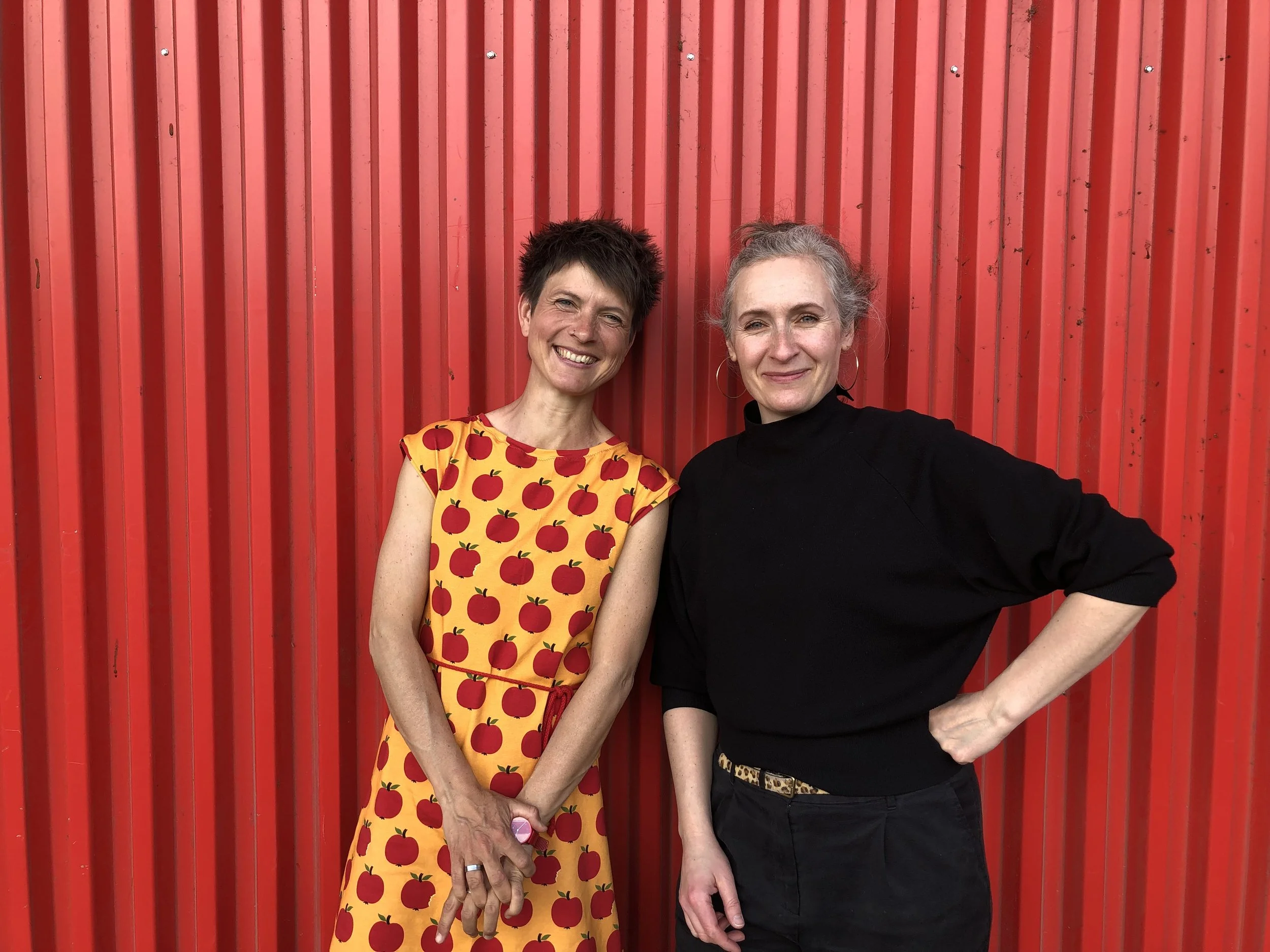 Judith und Larisa stehen vor einer knallroten Garage und grinsen.
