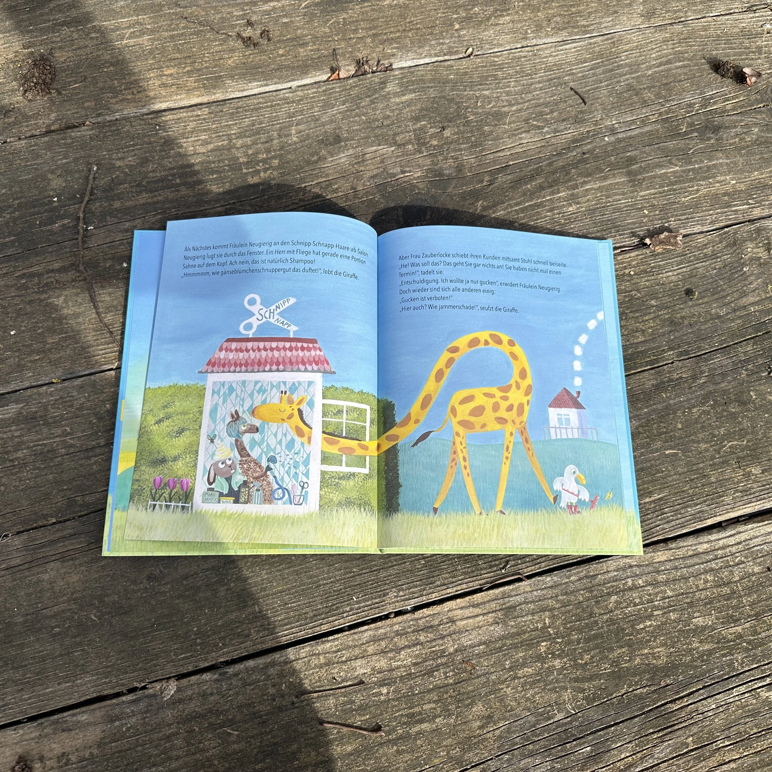 Das Foto zeigt eine Innenseite aus dem Bilderbuch "Fräulein Neuierig". Die neugierige GIraffe in den Schnipp-Schnapp-Haare-ab-Salon. Also einem Friseurladen.