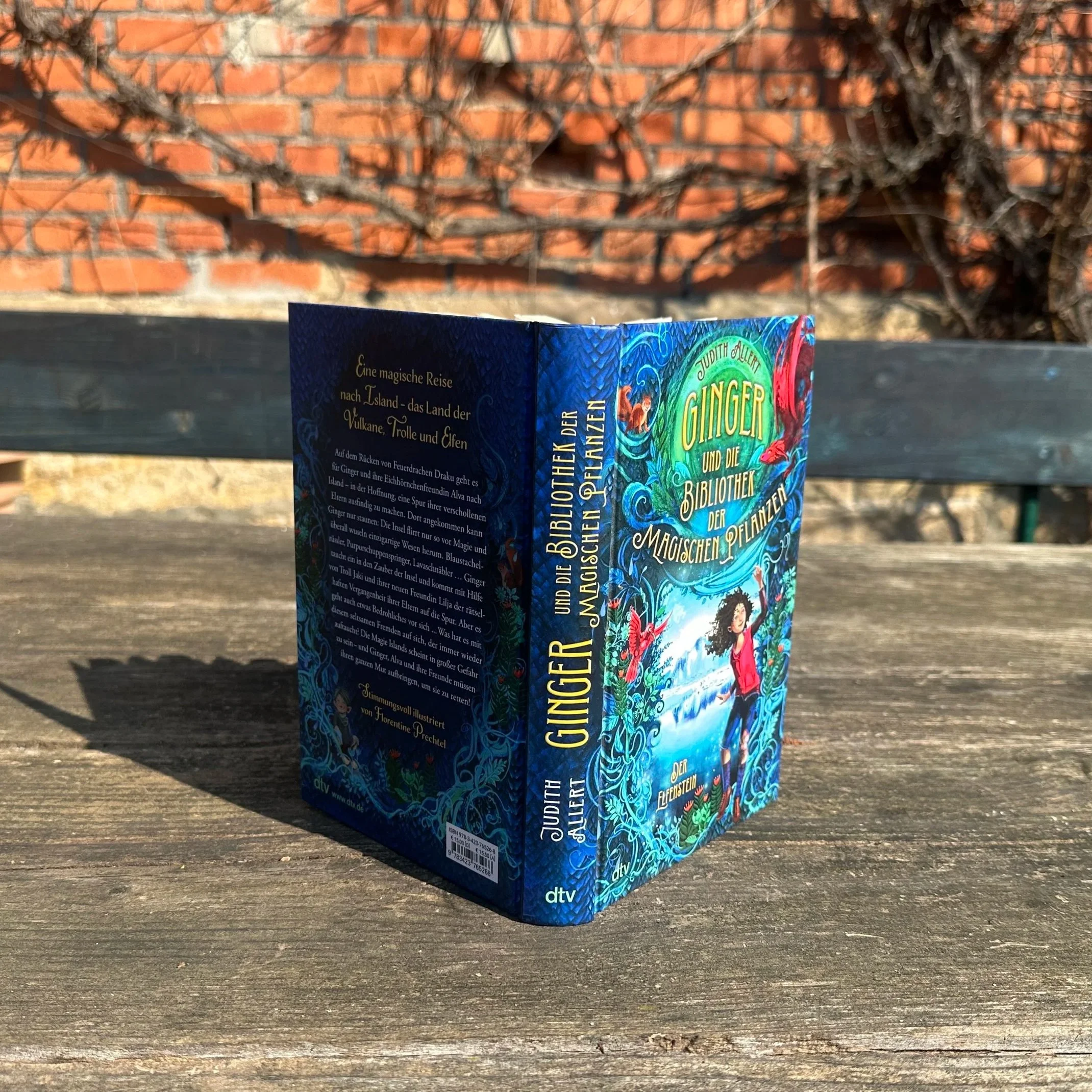 Das Buch "Ginger und die Bibliothek der magischen Pflanzen - der Elfeinstein" steht hochkant auf einem Tisch