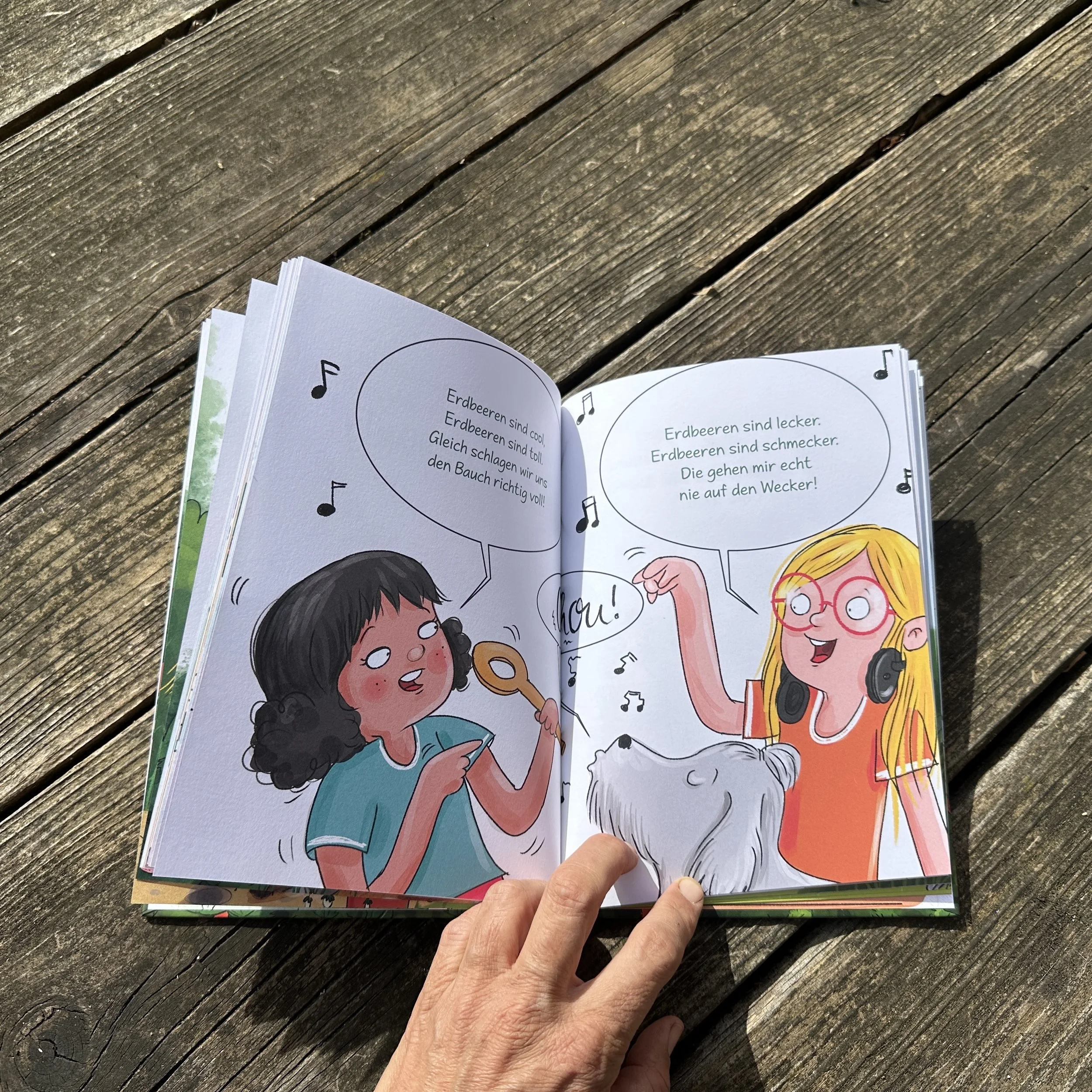 Das aufgeschlagene Buch "Die Erdbeermädchen". Bunt illustriert von Tessa Rath, mit einer Geschichte von Judith Allert