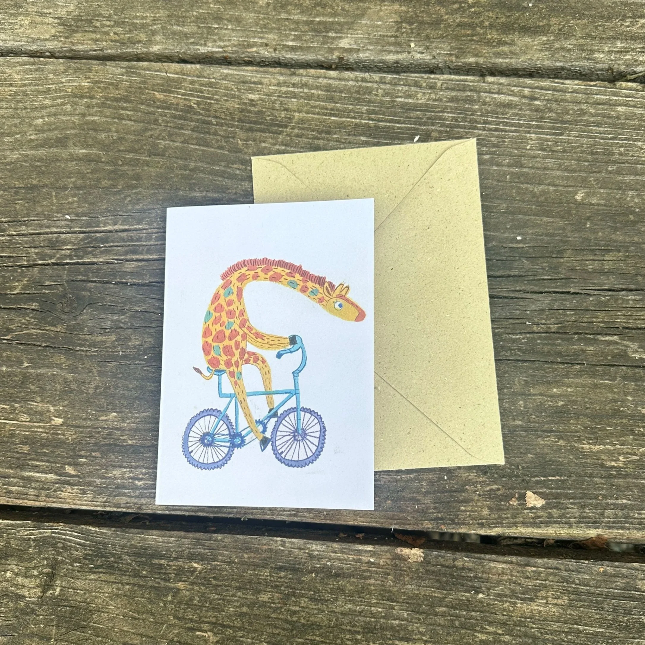 Die Grußkarte "Das Fräulein fahrt Rad" liegt mit einem Umschlag auf einem Tisch.