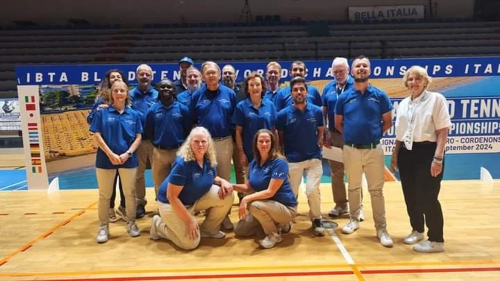 Circa 15 scheidsrechters poseren voor groepsfoto in blauwe t-shirts.