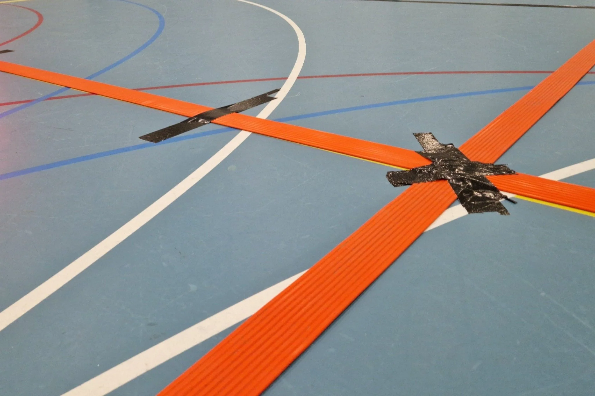 Rode voelbare lijnen vastgeplakt met zwart tape op een blauwe sporthalvloer. 