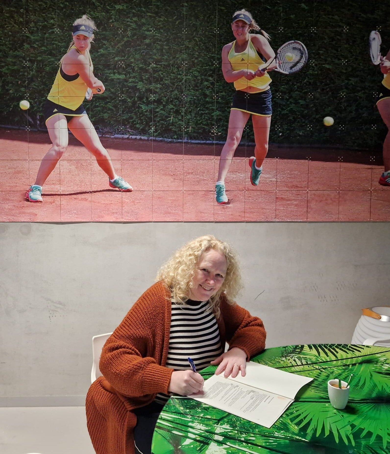 Fanny van den Heuvel ondertekent de statuten. Ze zit aan een groene tafel en lacht naar de camera. Op de achtergrond een poster met twee vrouwelijke tennisser in actie.