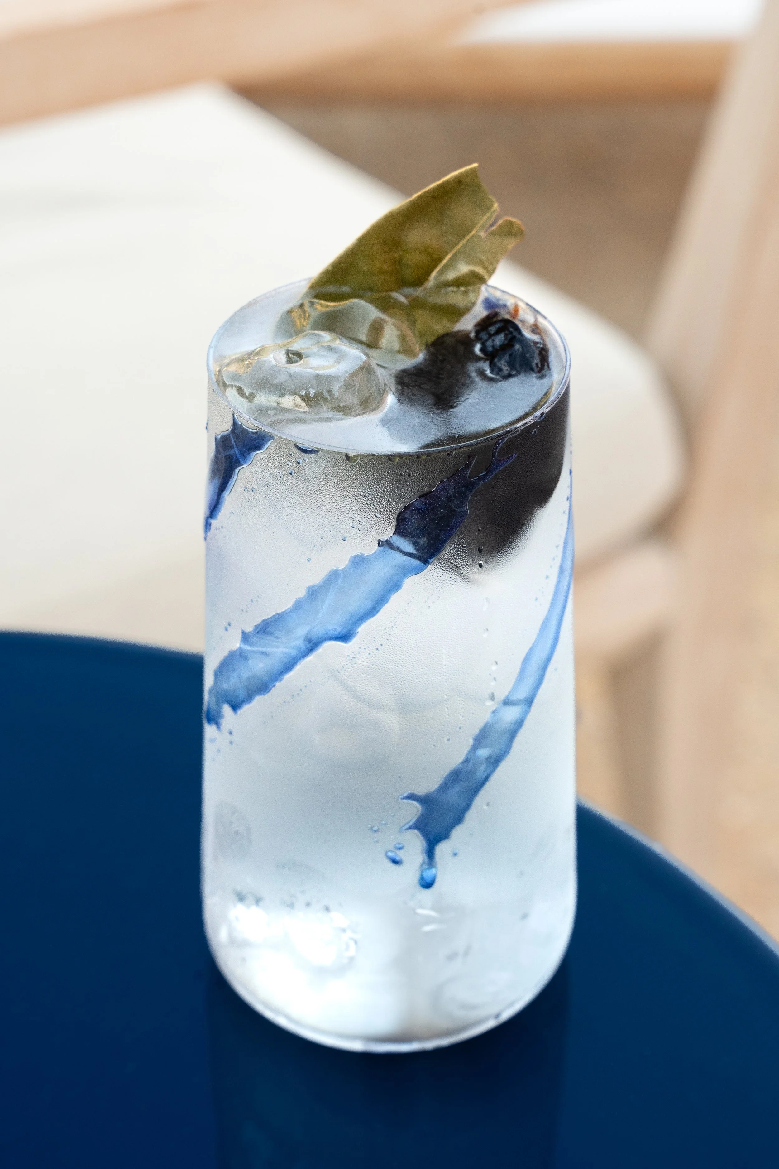 Un bicchiere trasparente con decorazioni di blu, riempito con acqua e ghiaccio, e una fetta di limone o lime sulla superficie.