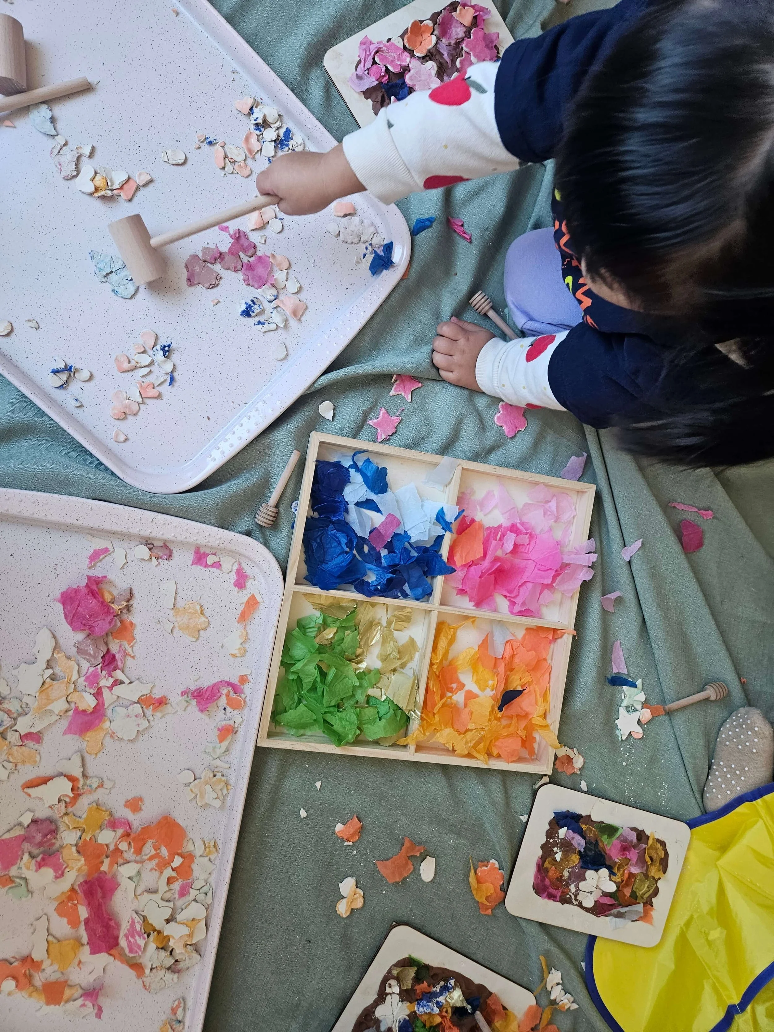 Toddler developing fine motor skills using a wooden mallet during sensory play