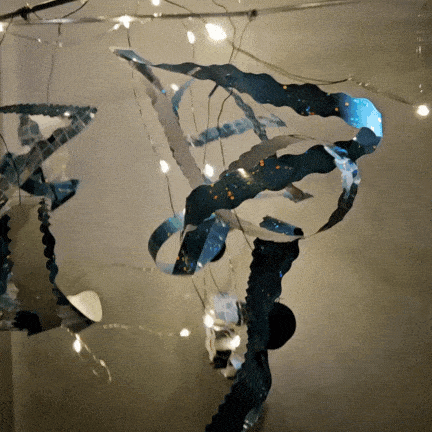 Decorative metal wind chimes hanging with string lights at night.