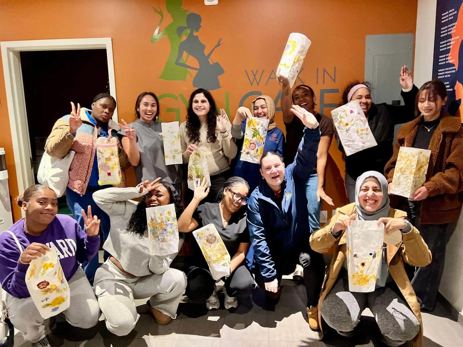 Group of diverse women gathered indoors, smiling and holding gift bags decorated with floral designs, celebrating together.