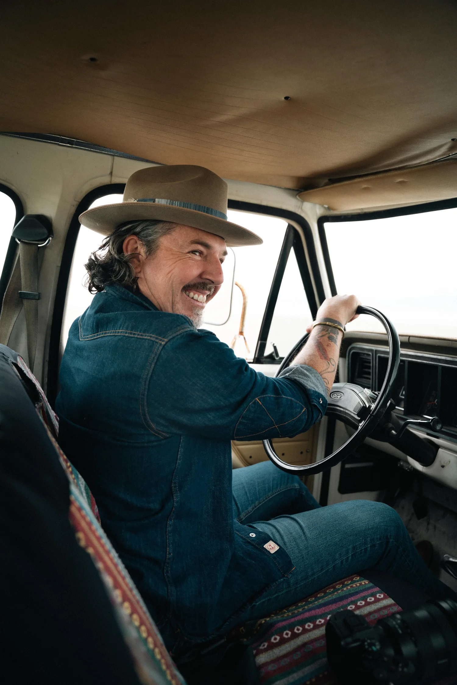 Neil Broere smiling over his shoulder from the driver's seat of an old truck