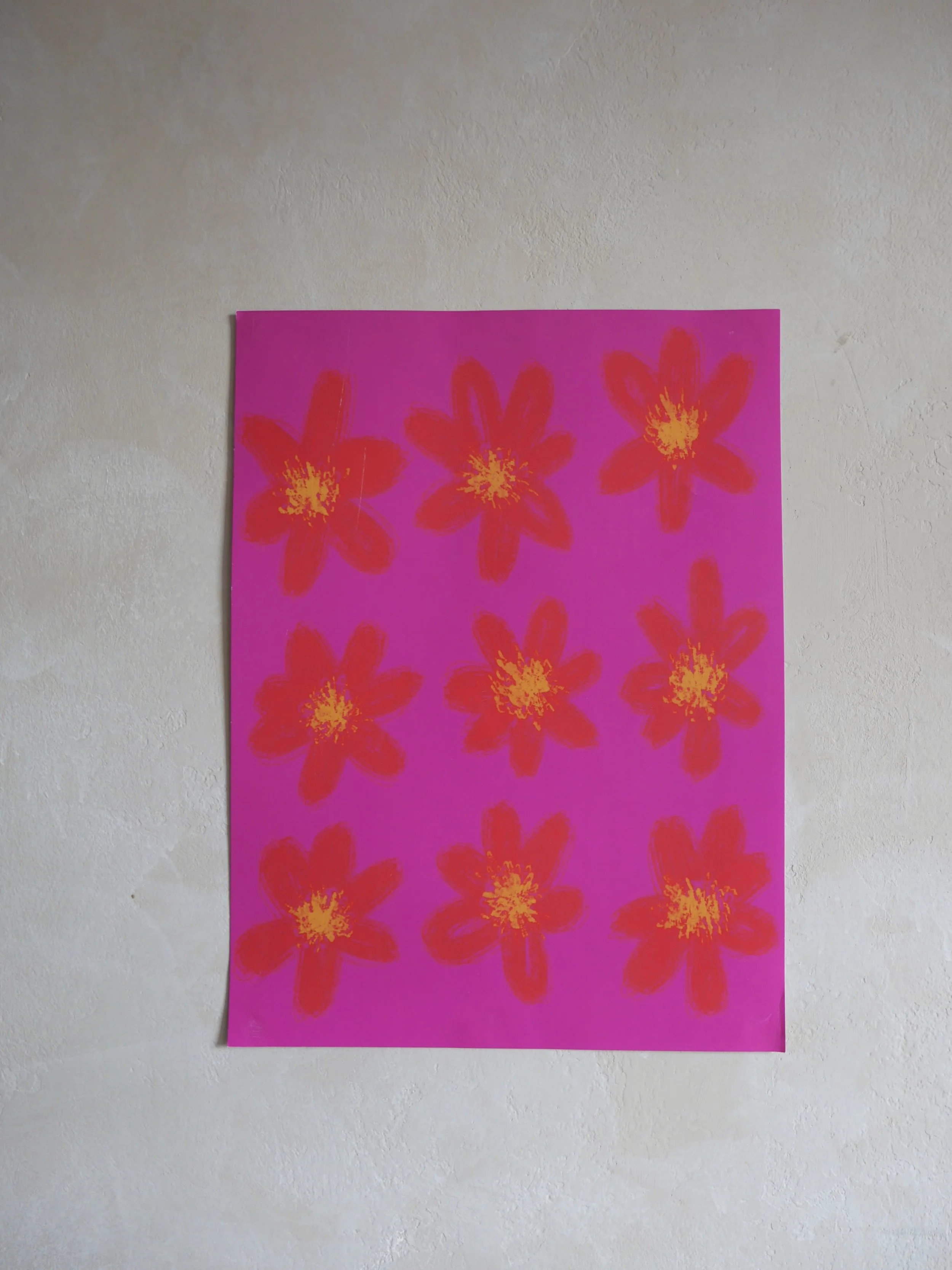Bright pink poster with red flowers and yellow centers, taped to a white wall.