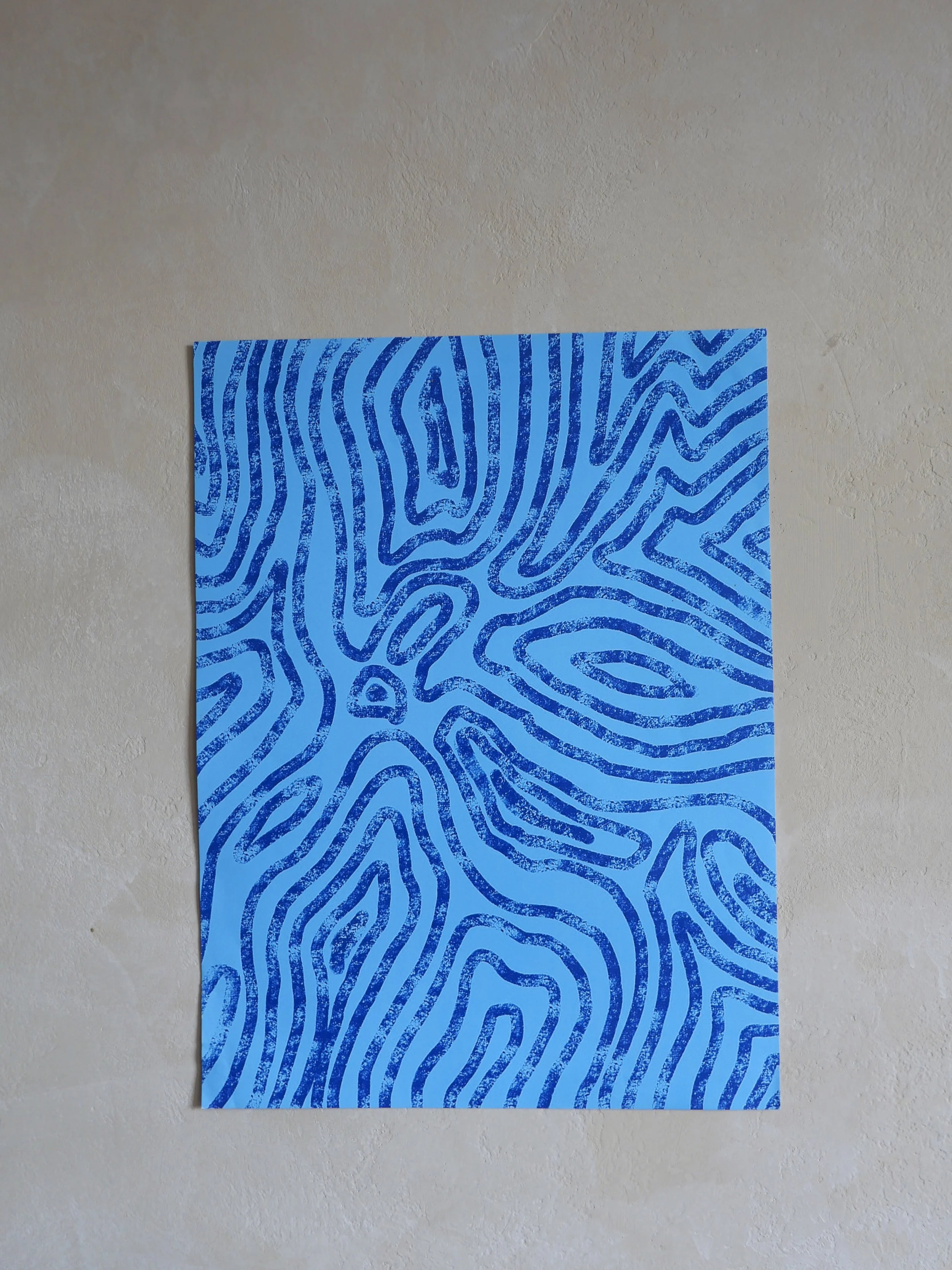 A piece of wall art with blue abstract maze-like lines on a blue background, mounted on a beige wall.