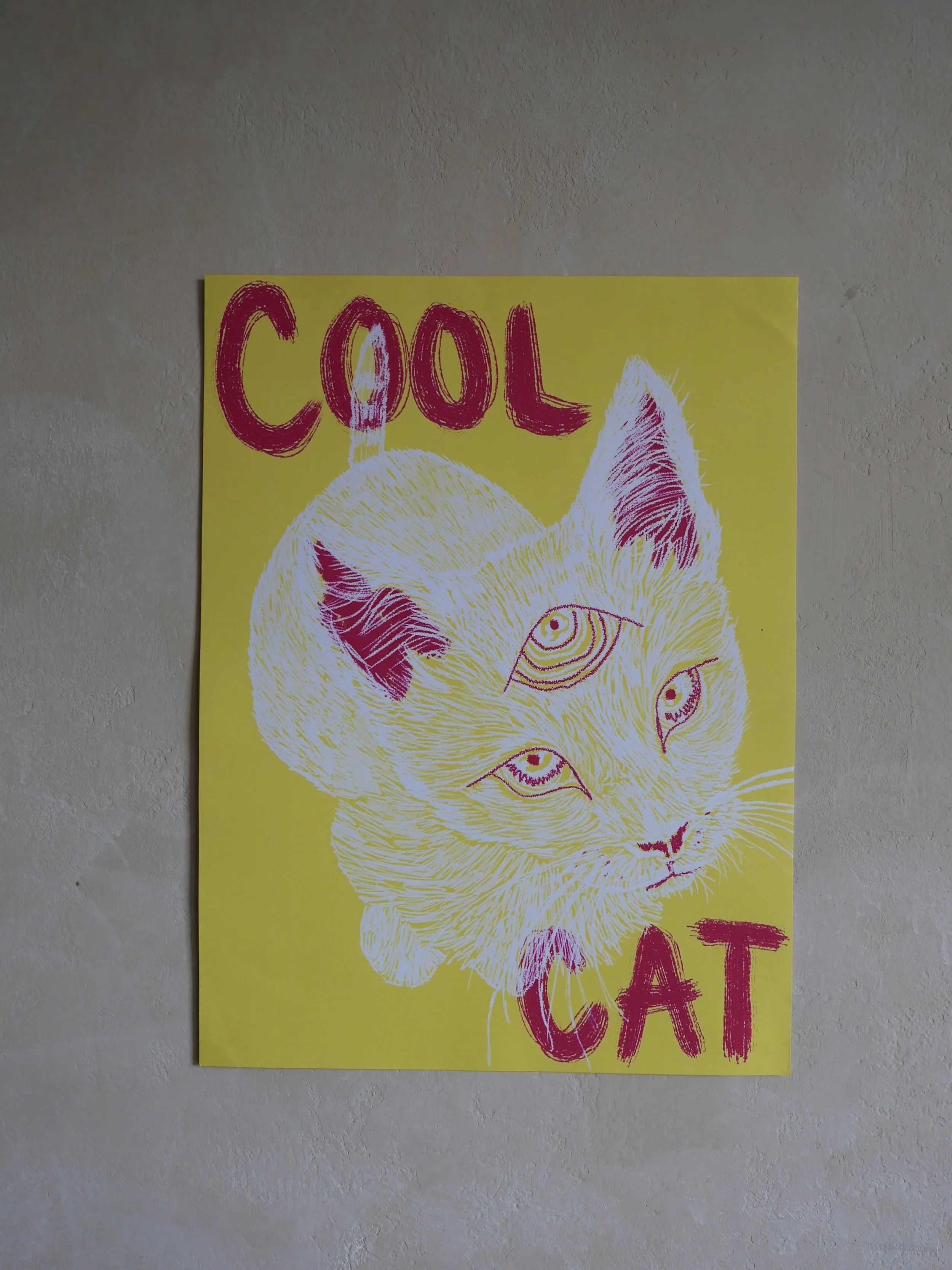 A yellow poster with the words 'COOL CAT' written in large pink letters and a drawing of a cat with three eyes.