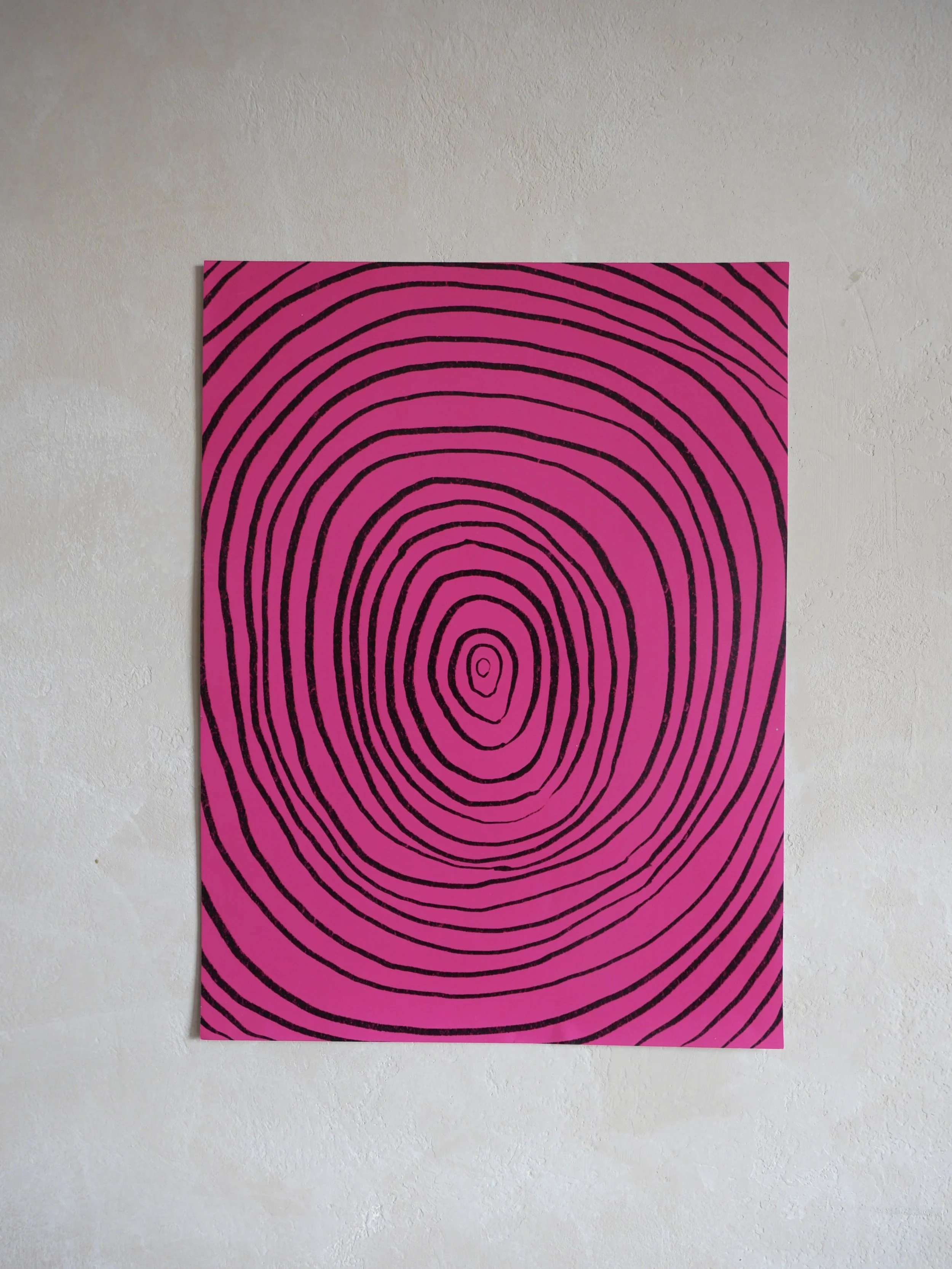 Pink and black abstract artwork featuring concentric irregular oval lines on a white wall.