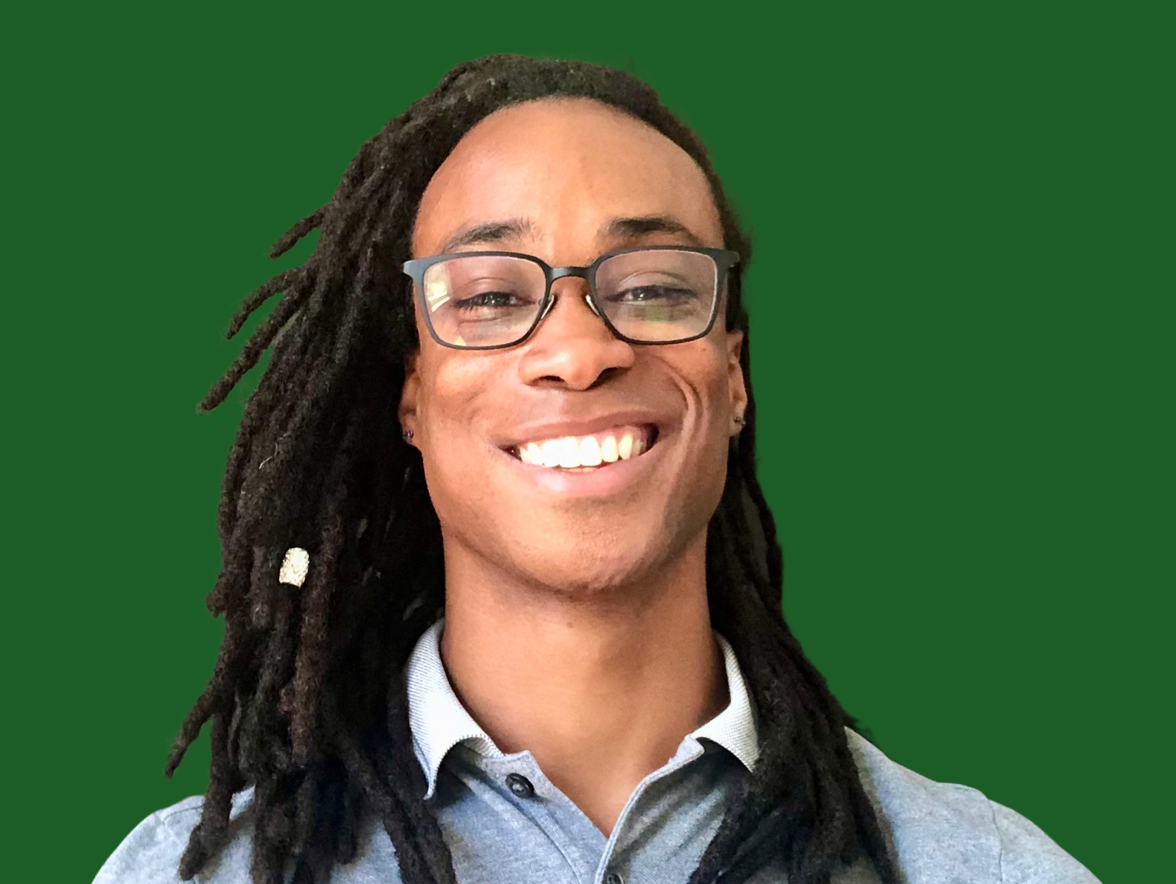 Person with dreadlocks wearing glasses and a gray shirt smiling against a green background.