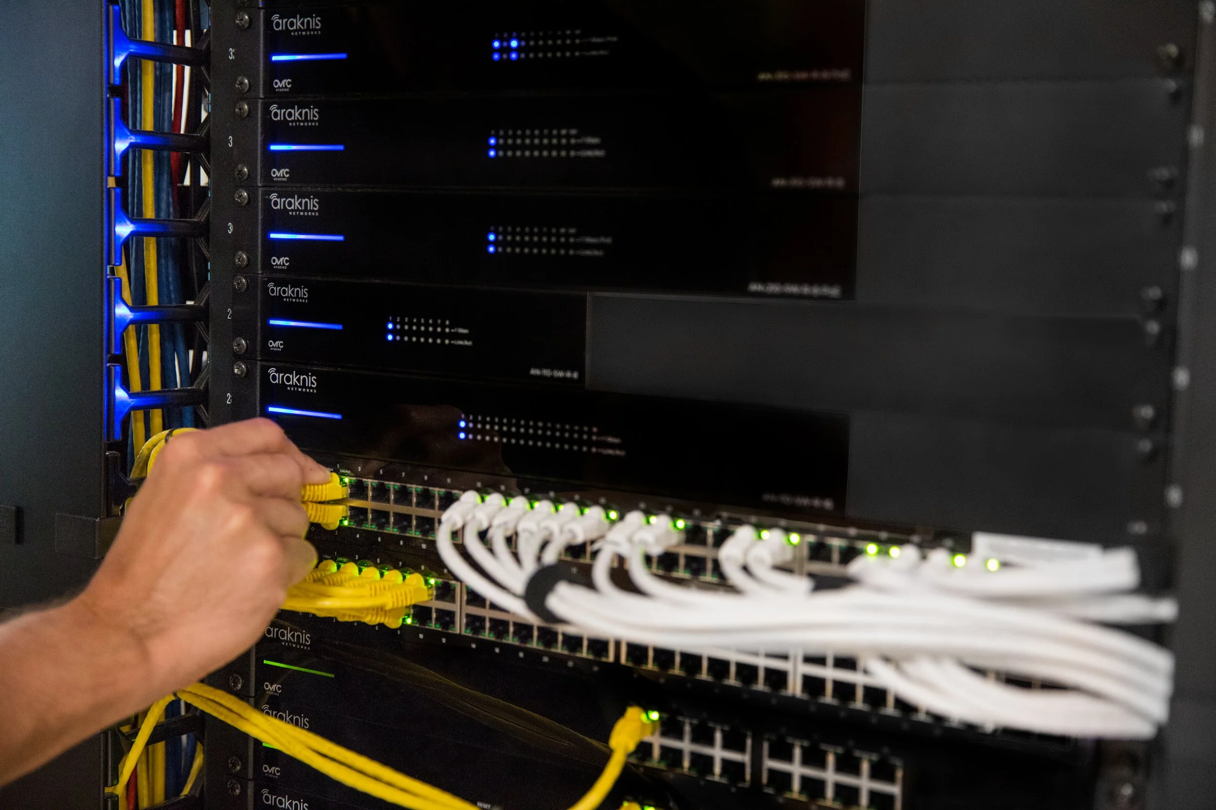 Person handling network cables in a server rack with Araknis devices.