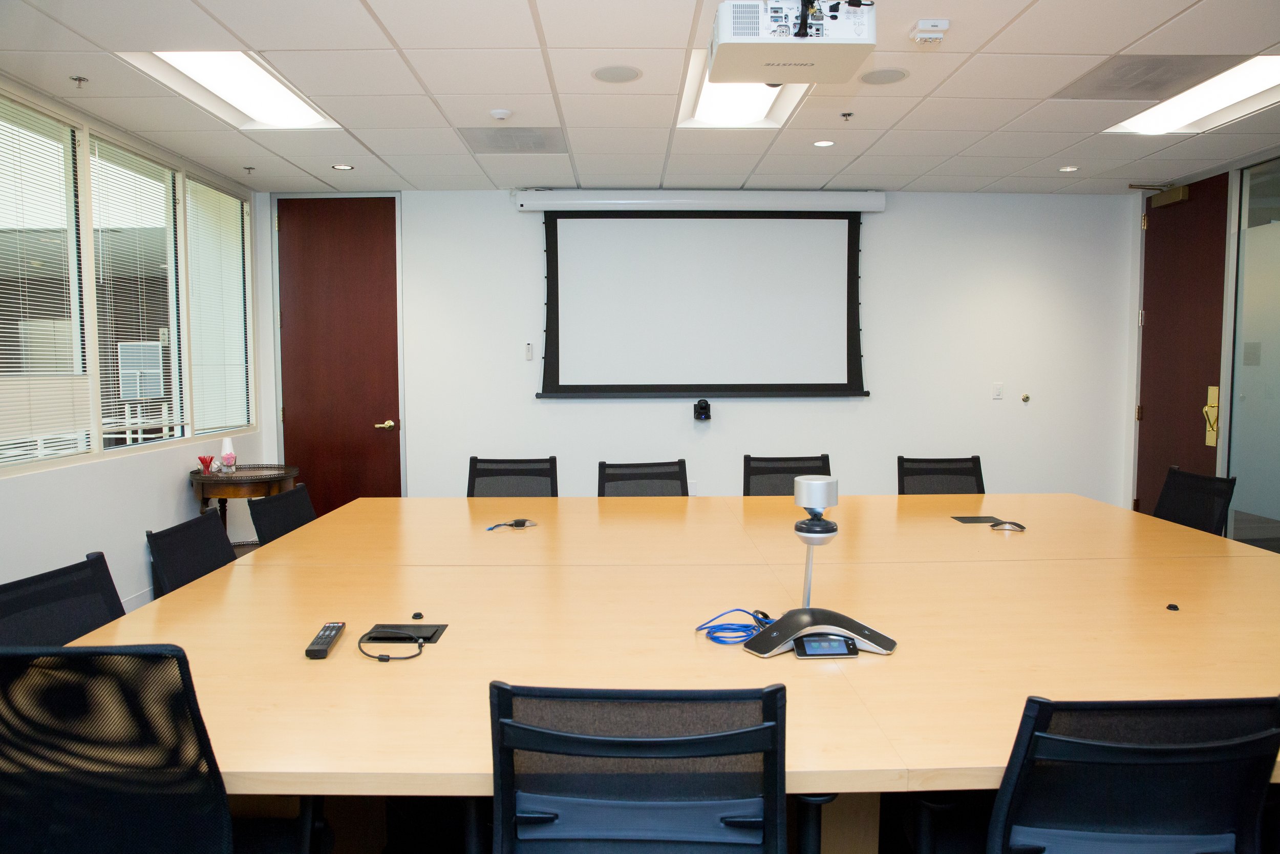 Empty conference room with a large table and chairs, projector, and screen