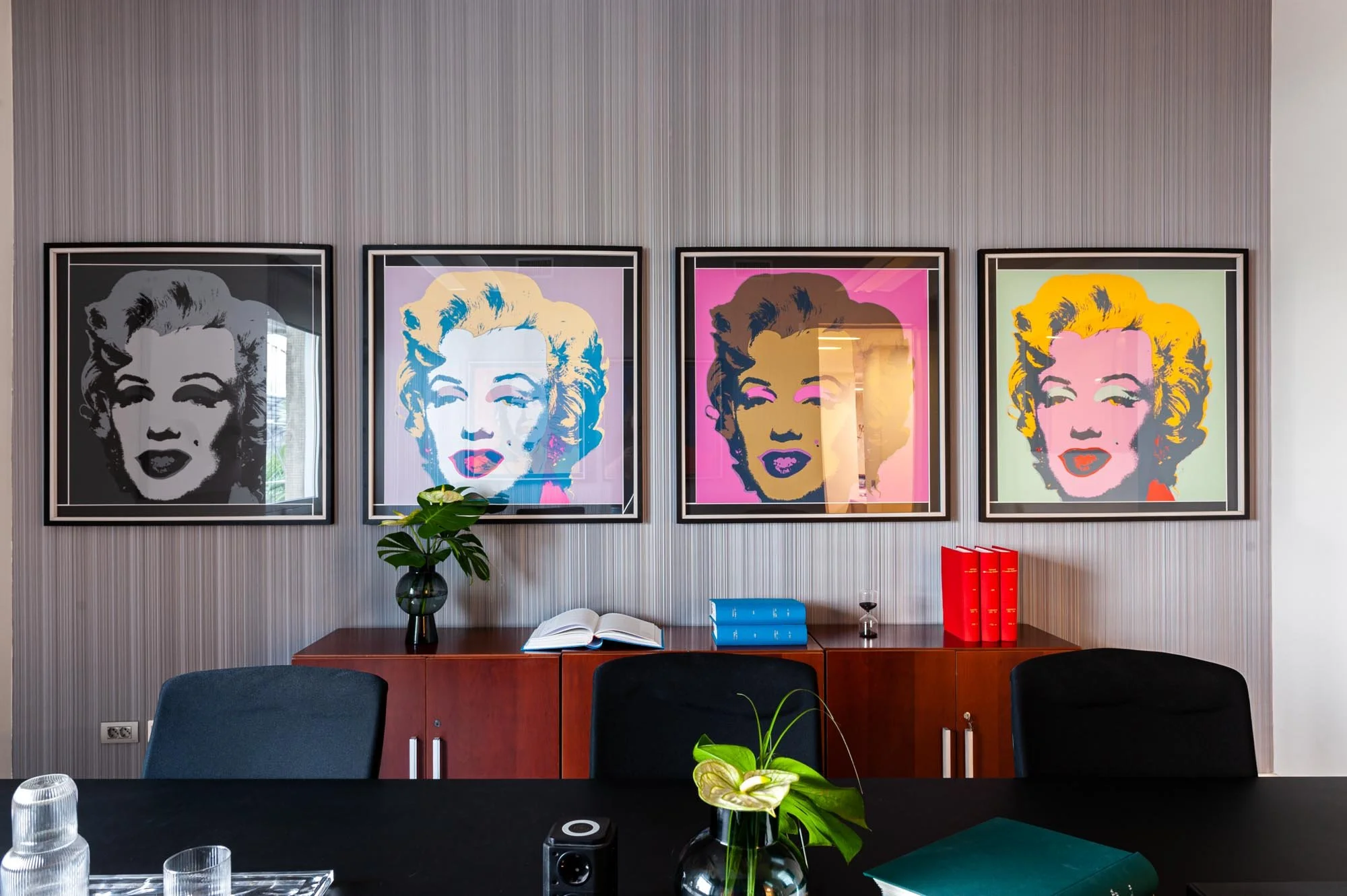 Stanza con quattro stampe pop art di un volto famoso appese al muro, sopra una credenza con libri e piante.