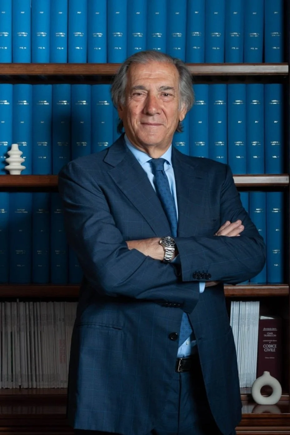 Uomo in abito davanti a una libreria con libri blu.