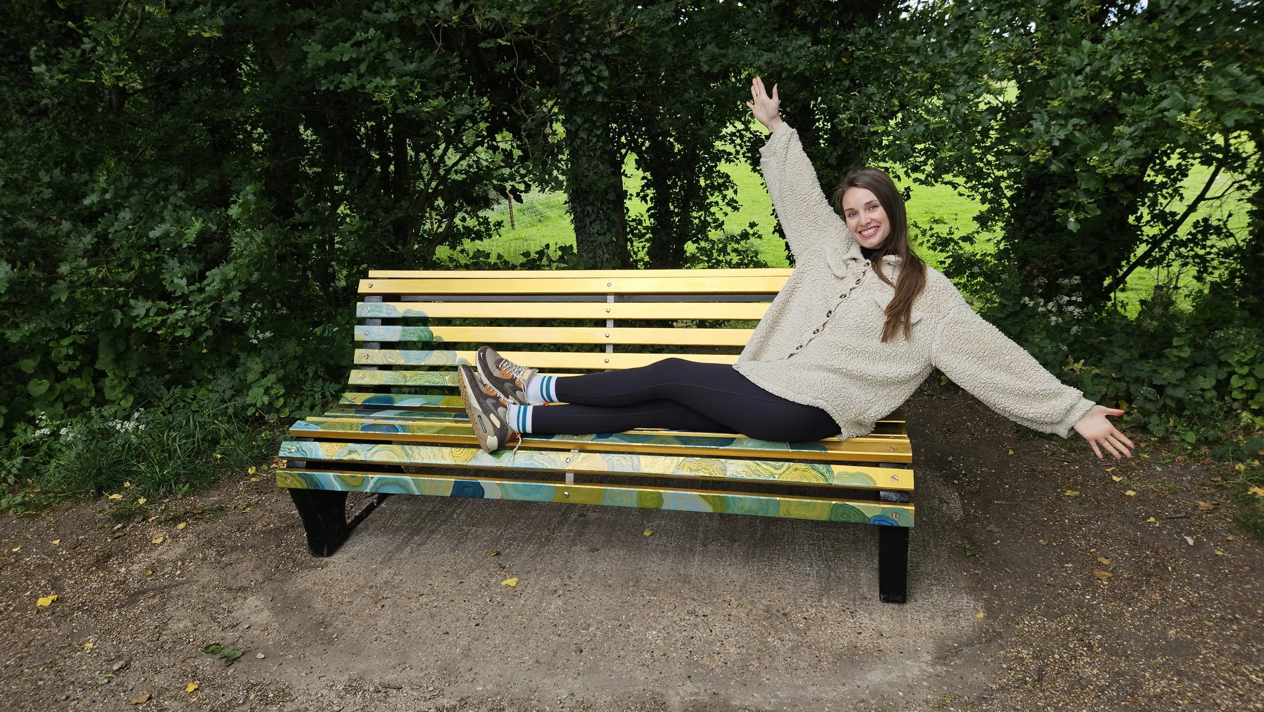 Jade sitting on her golden bench with arms up in the air. This bench is part of the river lea art trail project