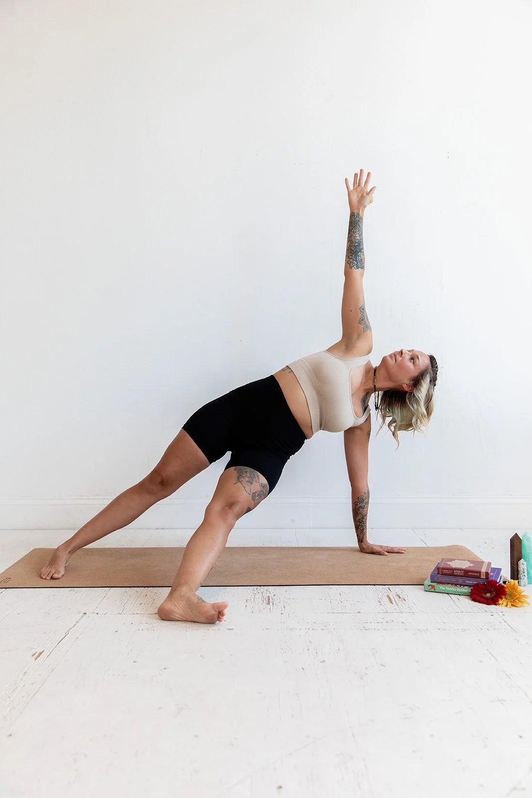 Woman practicing yoga in a side plank pose on a yoga mat with books and flowers nearby.
