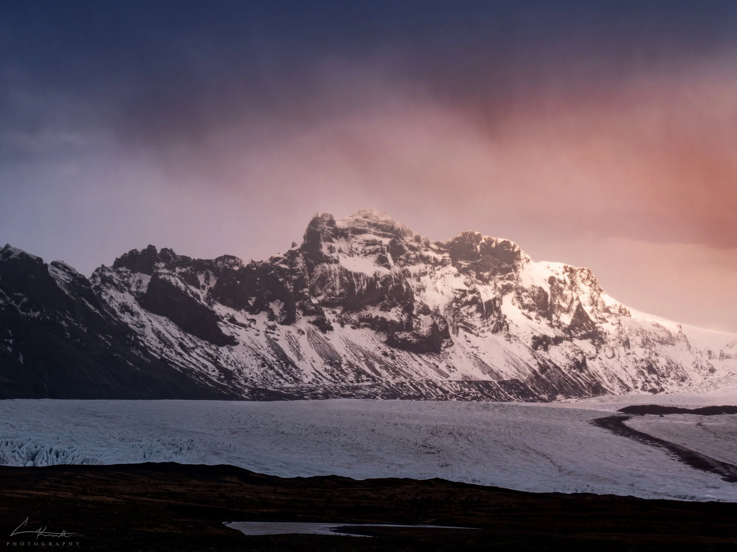 Golden pink sunrise lighting up snow-covered mountain peaks above the Jökulsárlón glacier in Iceland.