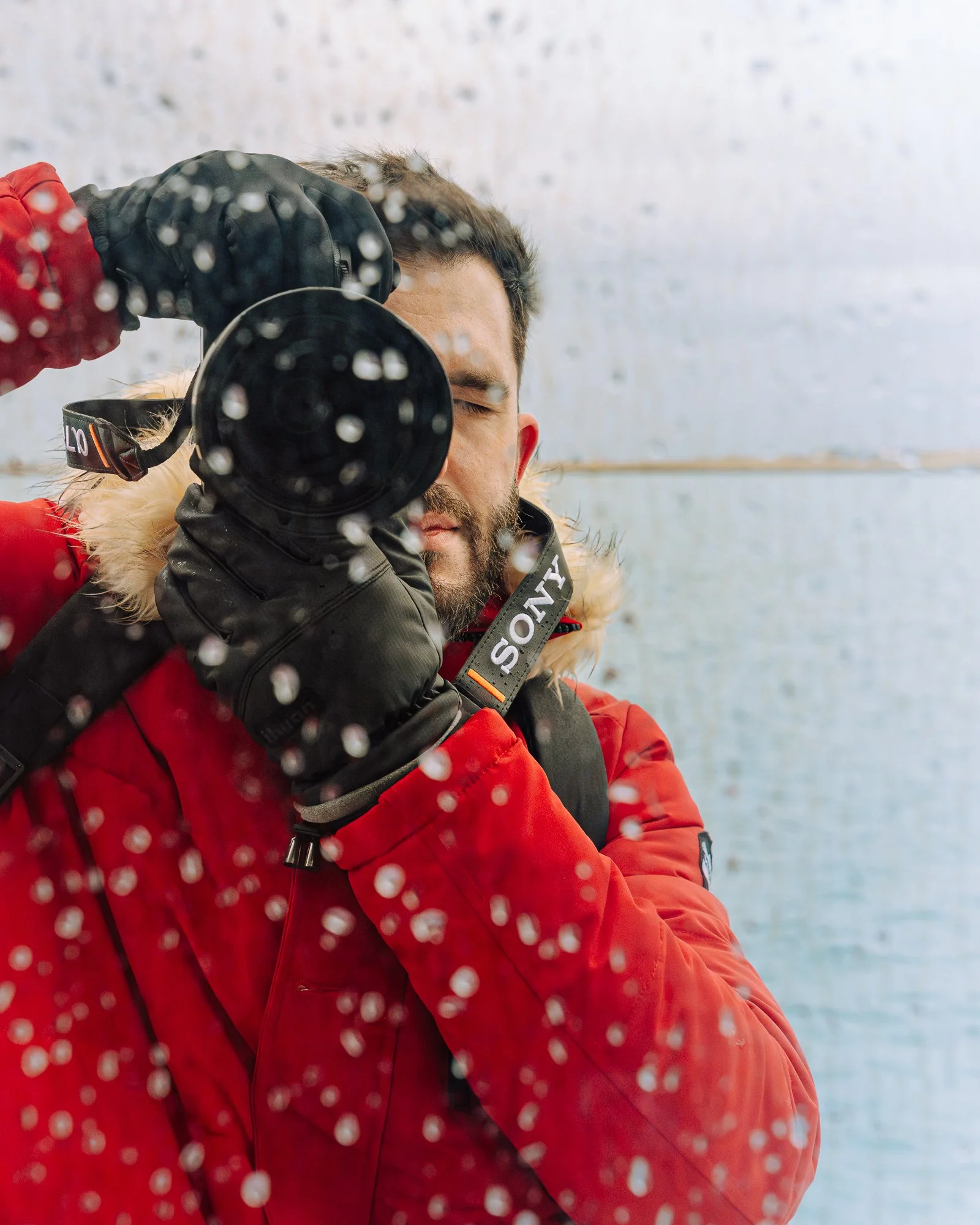 Photographer in red parka taking a picture through a rainy window.