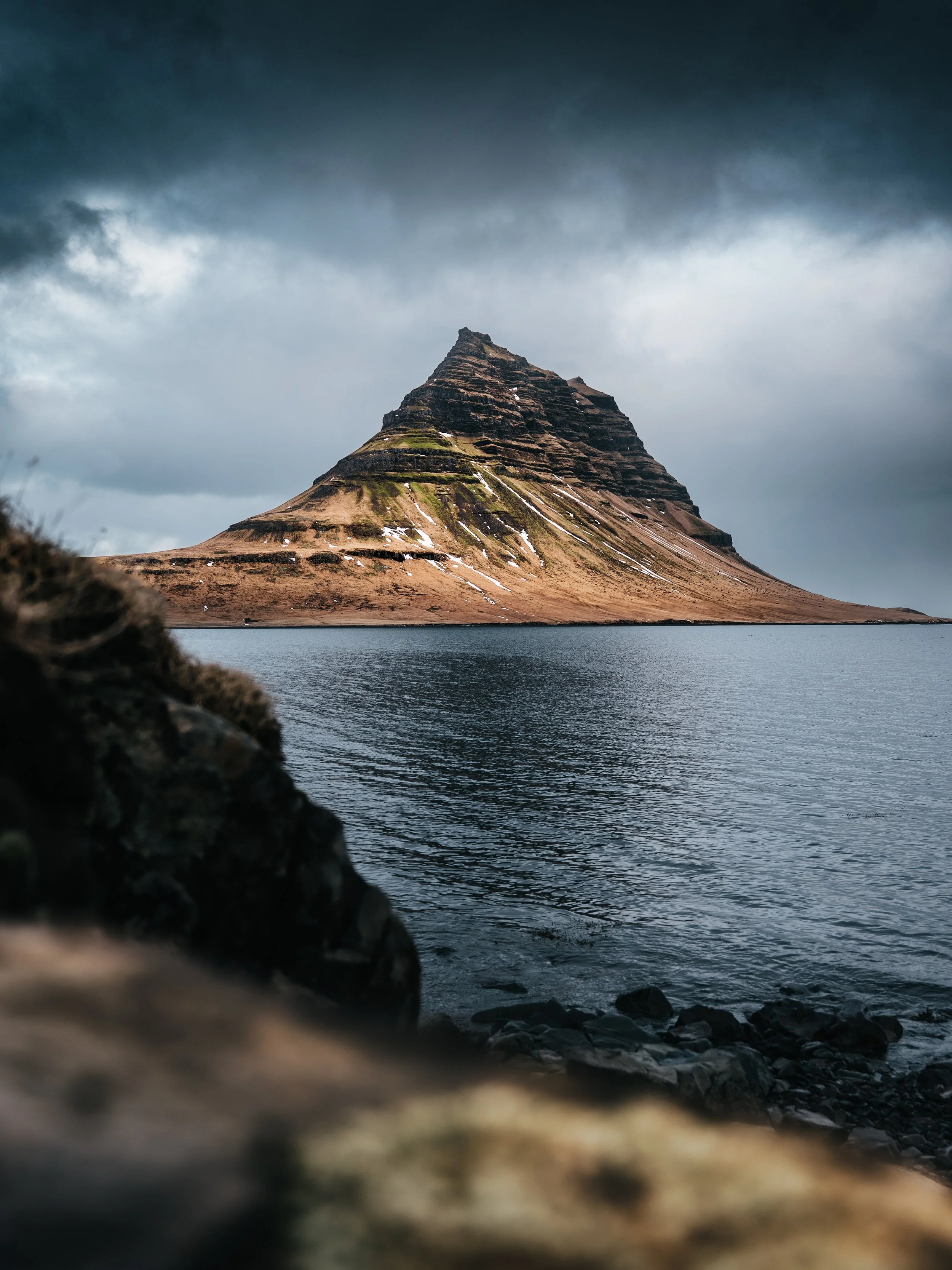 Kirkjufell mountain standing out boldly against dark, moody, stormy skies.