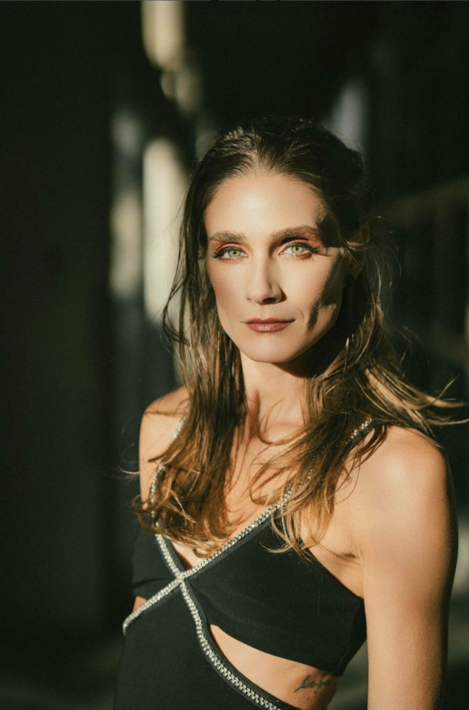 Woman wearing a black top with a serious expression, standing in dramatic lighting.