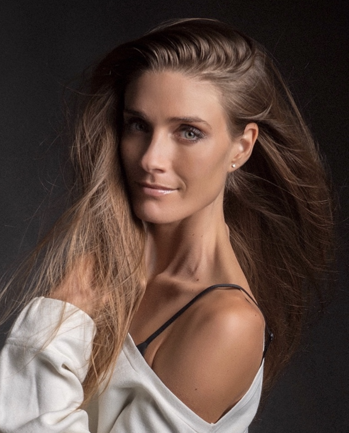 Close-up of a woman with long hair wearing an off-shoulder top on a dark background.