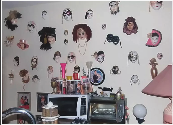 Decorative wall with numerous vintage masks and dolls, a microwave oven, and various household items including lamps, vases, and cups.