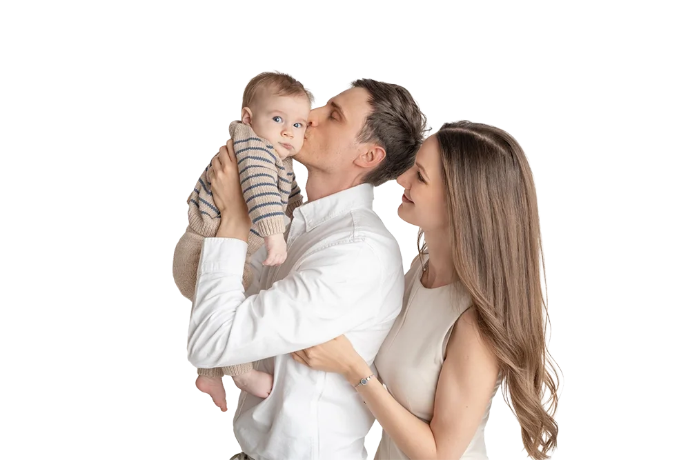 Vater küsst sein Baby auf die Wange, während die Mutter lächelnd danebensteht.