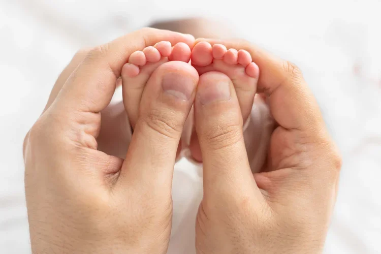 Kleine Babyfüße werden beim Newborn Shooting behutsam in beiden Händen gehalten.