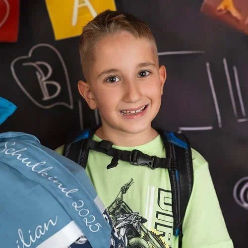 Lächelnder Junge trägt seinen Schulranzen und hält eine blaue Schultüte.