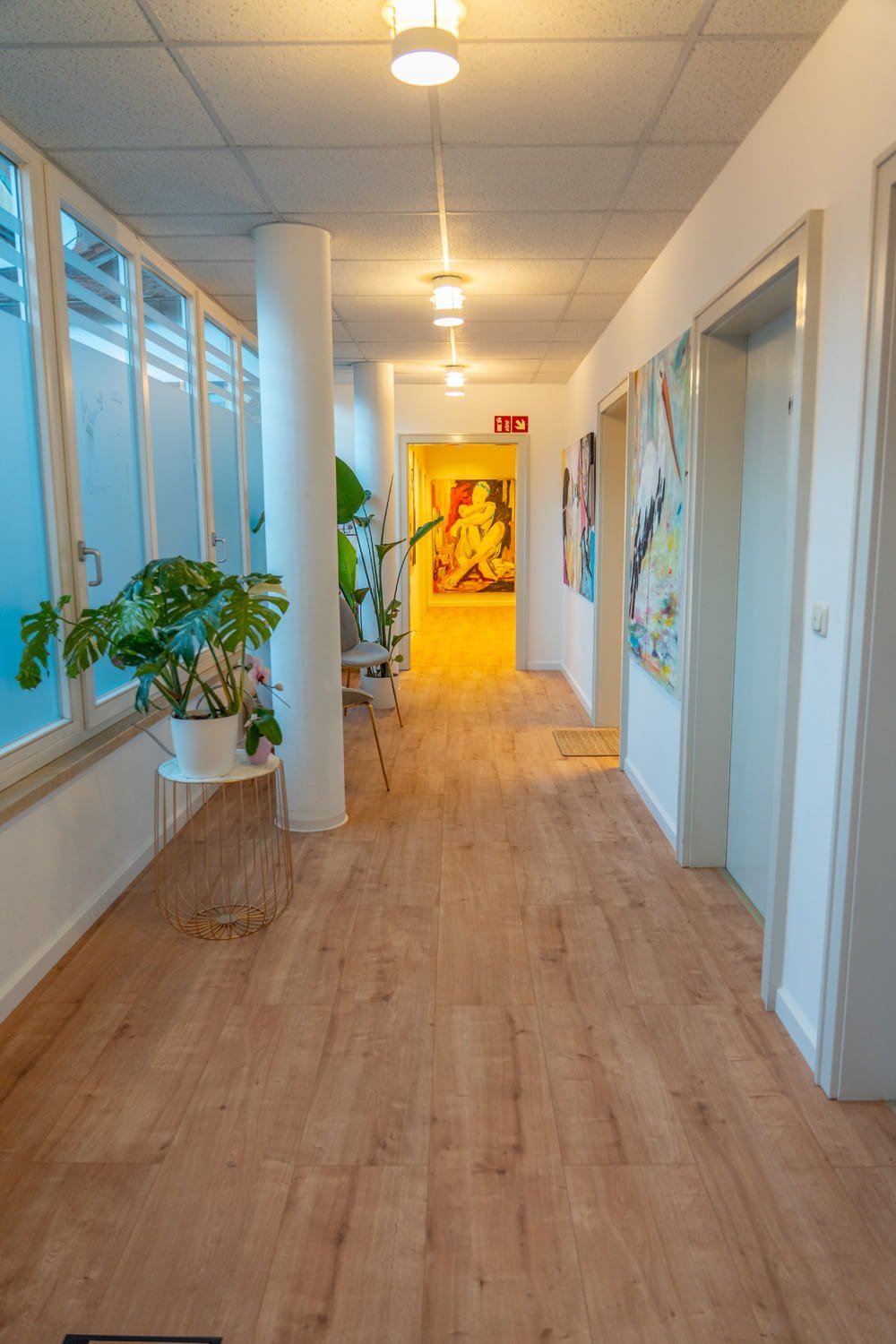 Ein Flur in einem Gebäude mit Holzfußboden, weißen Wänden und dekorativen Kunstwerken.