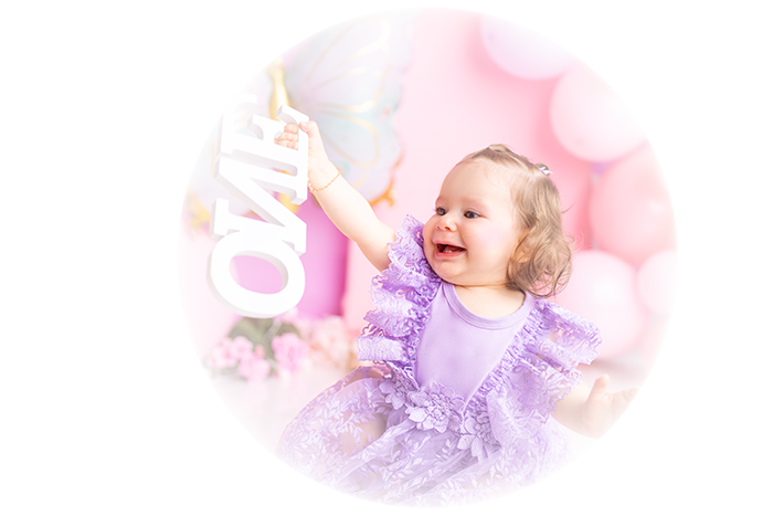 Lächelndes Baby in lila Kleid bei einer Feier, mit einem Hello Kitty-Poster im Hintergrund.
