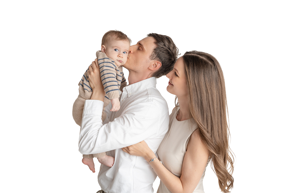 Familie mit Vater, Mutter und Kind, der Vater küsst das Kind auf die Wange, die Mutter schaut liebevoll zu ihnen, alle lächeln.