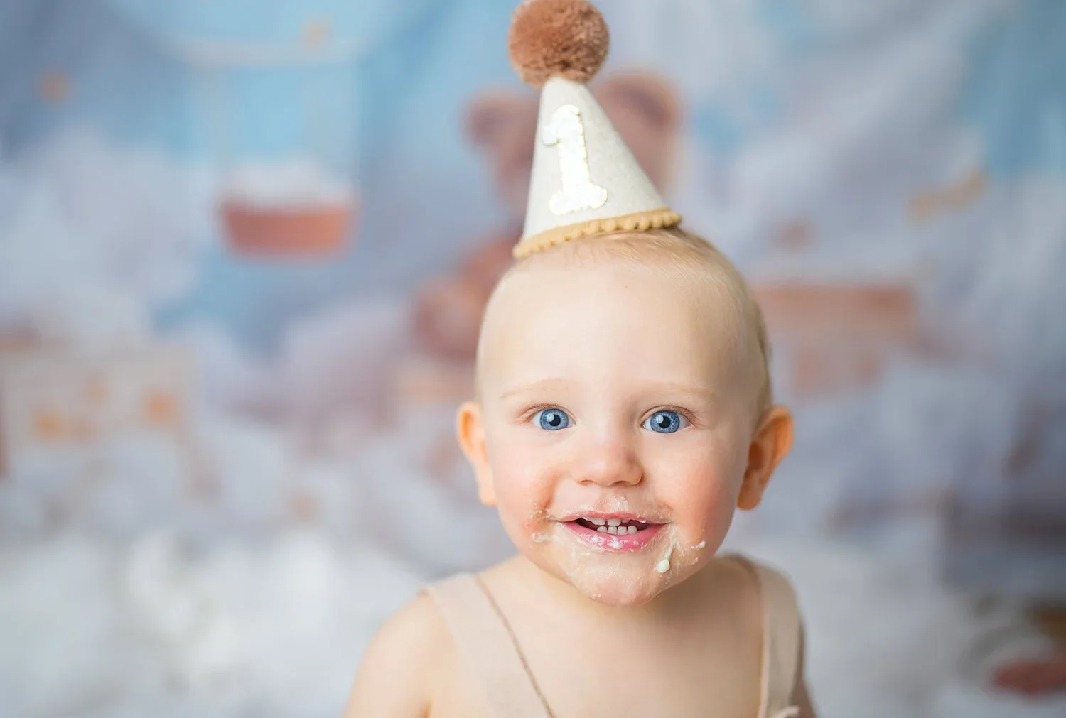 Lächelndes Baby mit Geburtstagshut und Tortencreme im Gesicht beim Cake Smash Shooting.