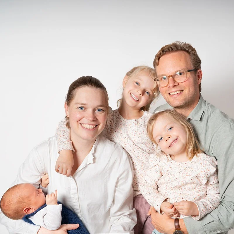 Eine glückliche Familie mit zwei kleinen Mädchen und zwei Erwachsenen, vor weißem Hintergrund.