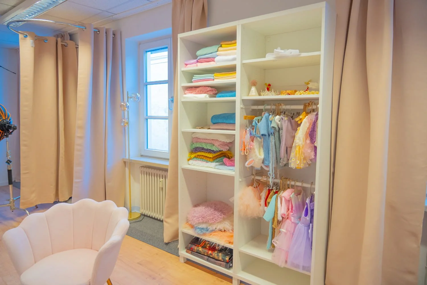 Regal mit gefalteten Handtüchern und Kinderkleidung, umgeben von beige Vorhängen und einem weißen Sessel.