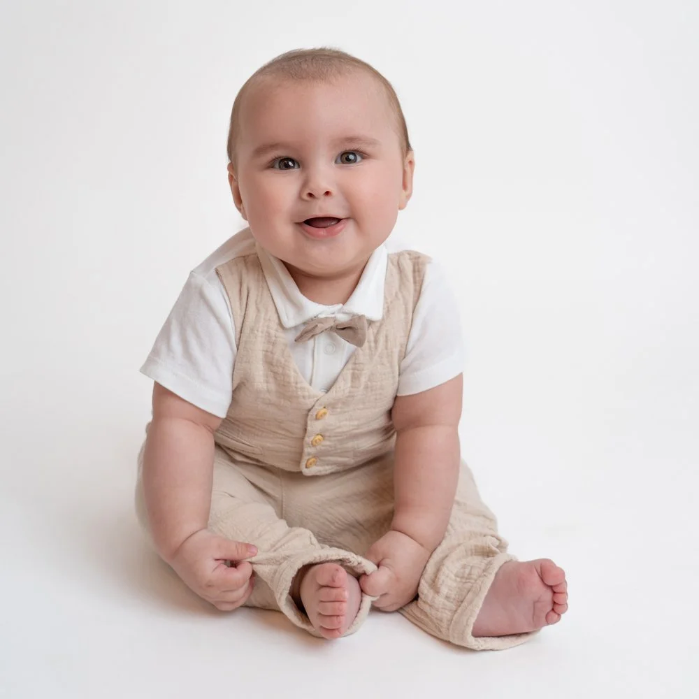 Süßer Babyjunge sitzt auf dem Boden, trägt beige Kleidung und lächelt freundlich.