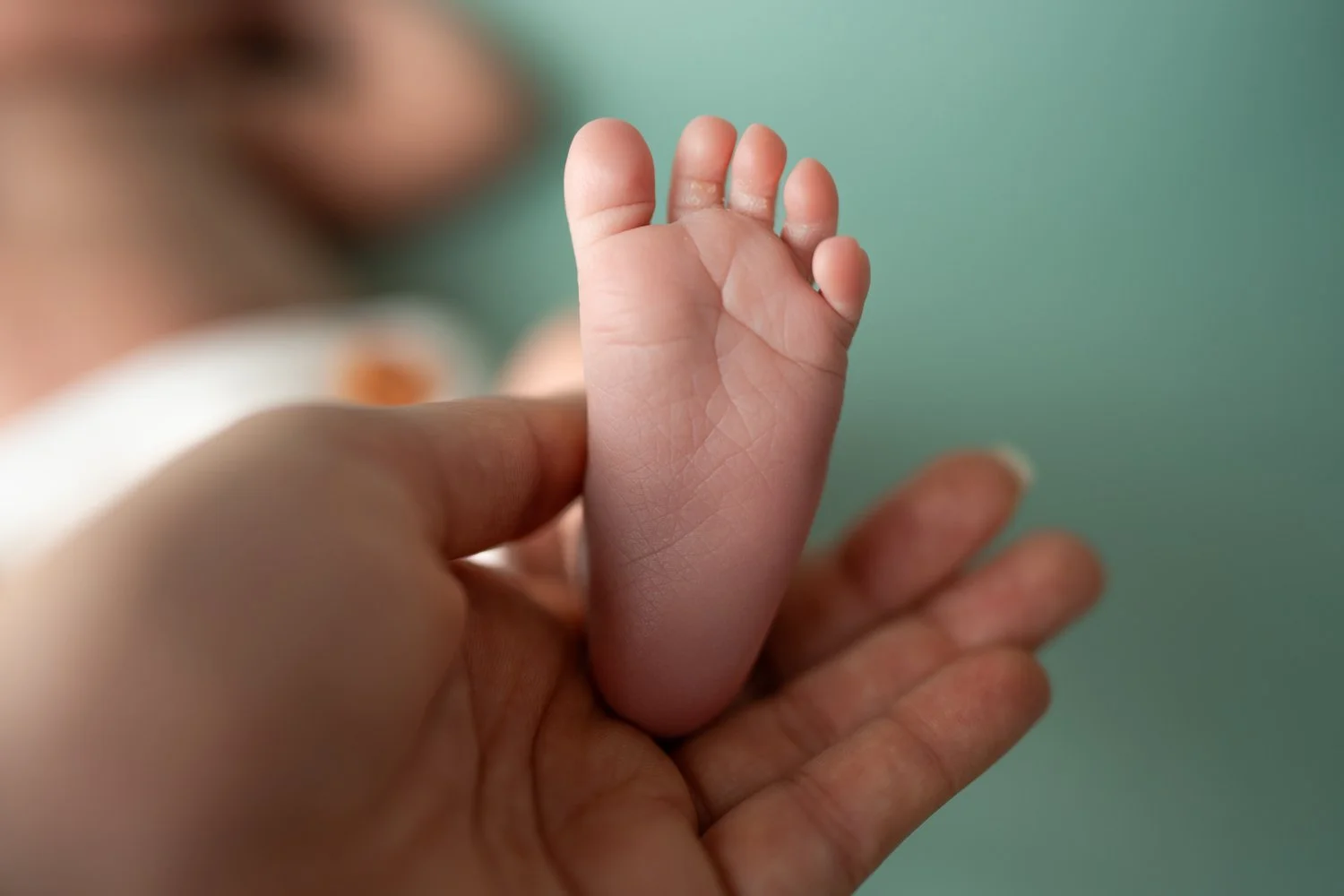 Nahaufnahme eines kleinen Baby-Fußes, der von einer Hand gehalten wird, mit einem grünen Hintergrund.