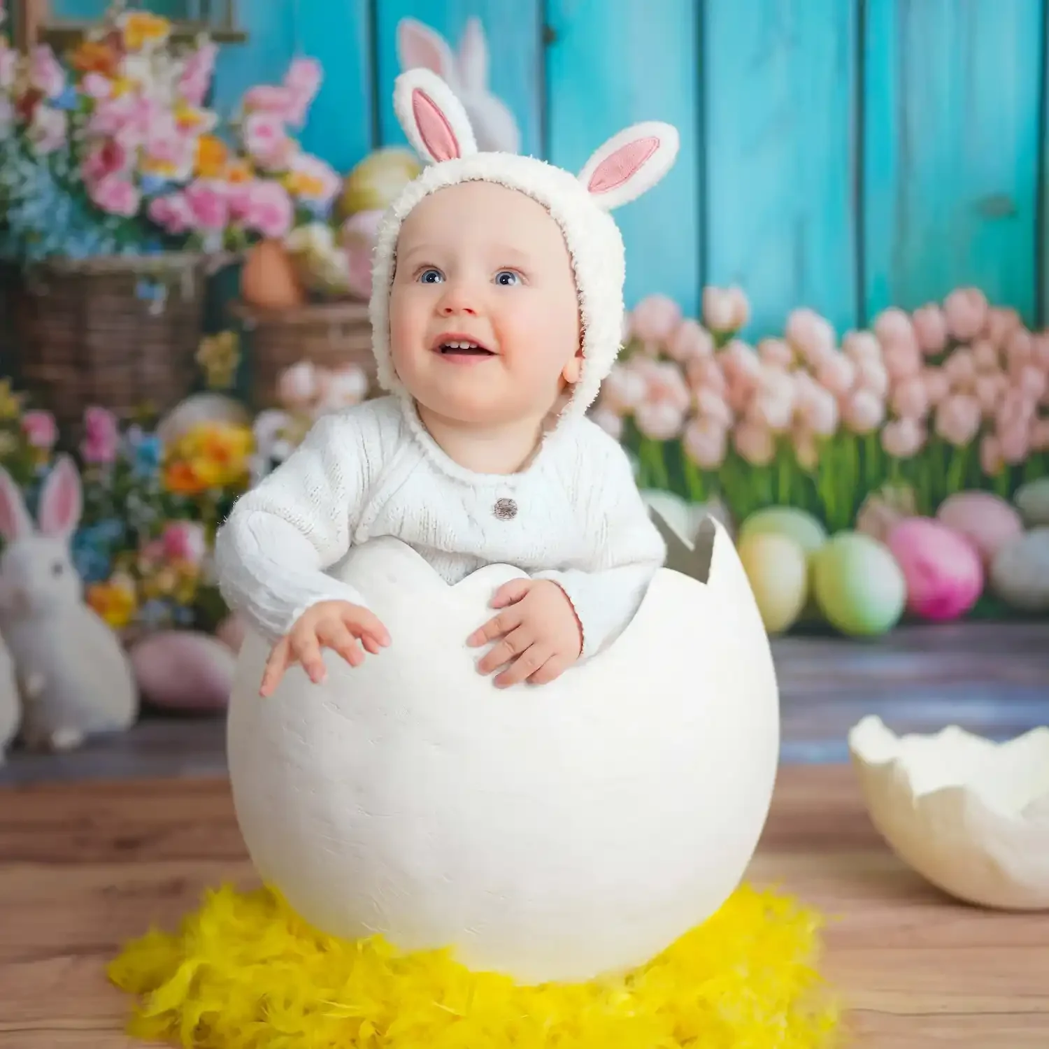 Lächelndes Baby mit Hasenmütze sitzt in einer weißen Eierschale.
