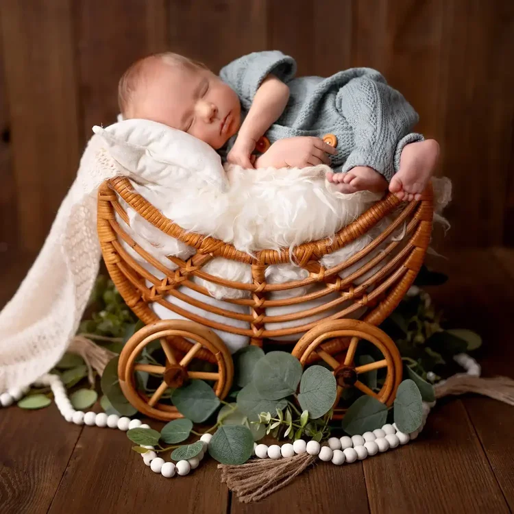 Schlafendes Neugeborenes in einem Rattan-Kinderwagen auf einer weichen weißen Decke.
