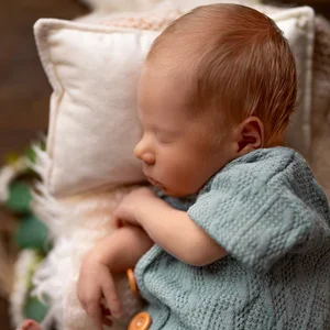 Schlafendes Neugeborenes liegt seitlich in einem grauen Strickoutfit.