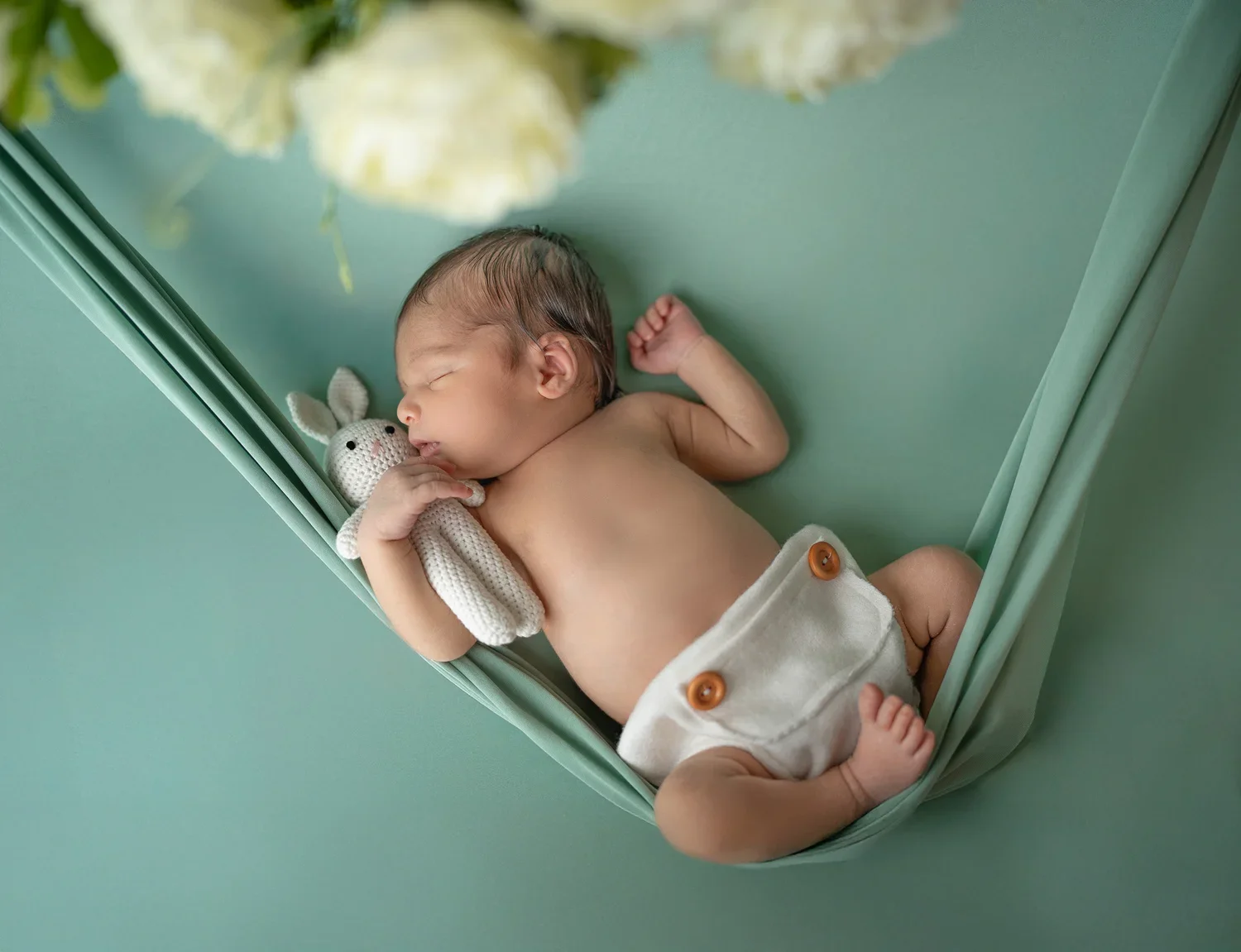 Kleines schlafendes Baby in einem Babybett, umarmt ein handgestricktes Hasen-Spielzeug.