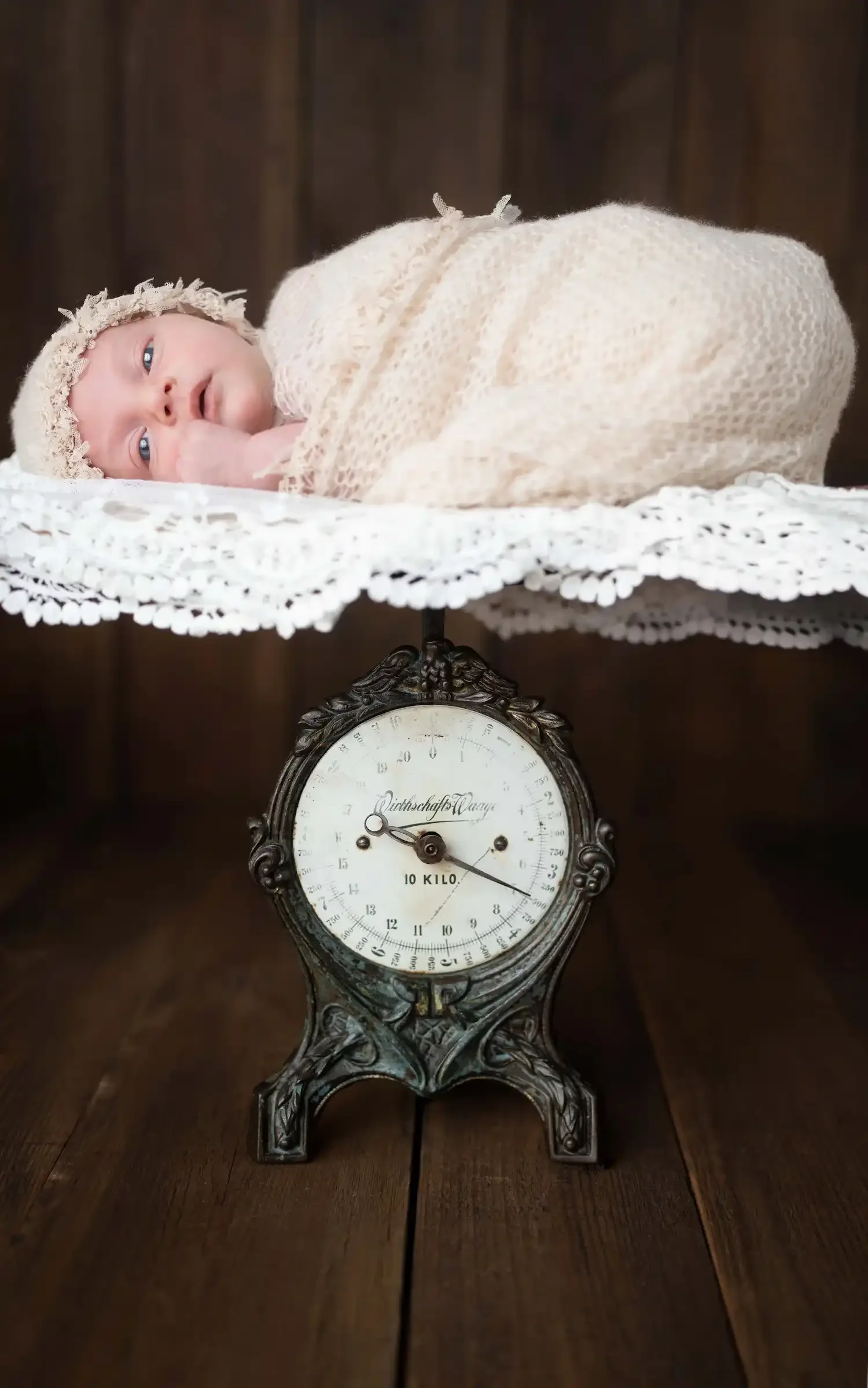 Eingewickeltes Neugeborenes schläft auf einer antiken Waage beim Newborn Shooting.
